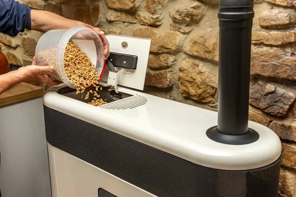 Person pouring wood pellets into a biomass heating system indoors.