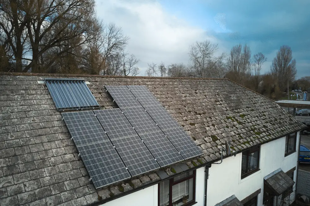 Roof of a house with solar panels and a solar thermal collector, demonstrating how to generate electricity at home using renewable energy sources.