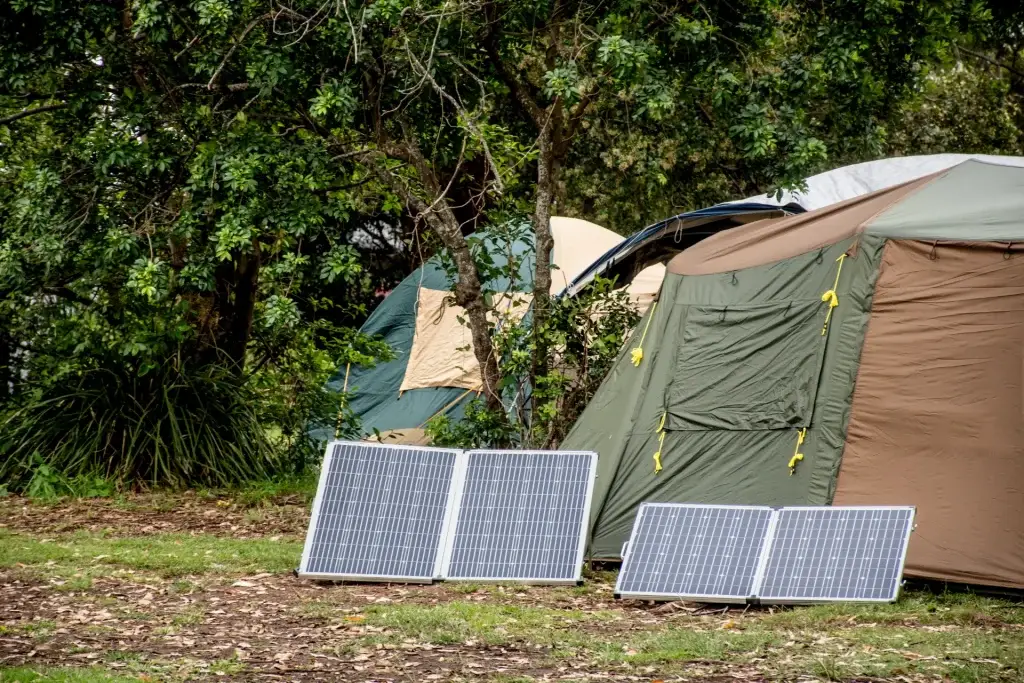 Portable solar panels set up outside a tent in a forested campsite.